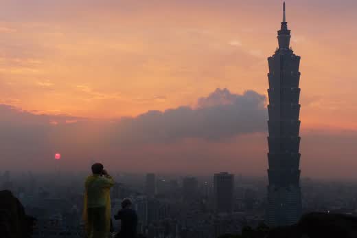Silueta del Taipei 101 al atardecer con dos personas fotografiando desde una roca