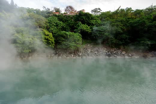 Estanque de agua verde humeante rodeado de vegetación en Beitou