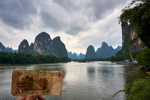 Billete de 20 yuanes sostenido frente al paisaje real del río Li