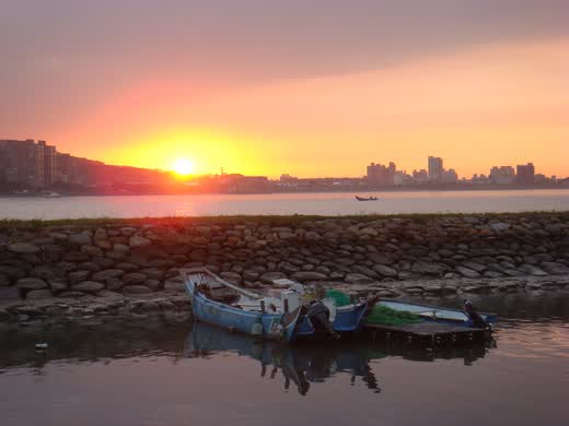 Atardecer naranja sobre el río Tamsui con barcas amarradas