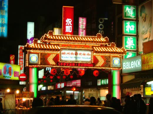 Arco iluminado de entrada al mercado nocturno de Raohe, de noche y con gente