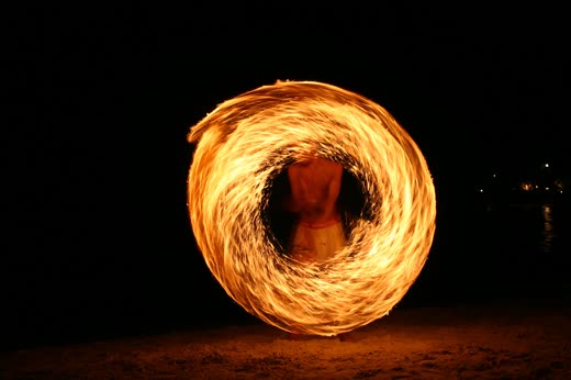 Bailarín girando un aro de fuego en la playa de noche